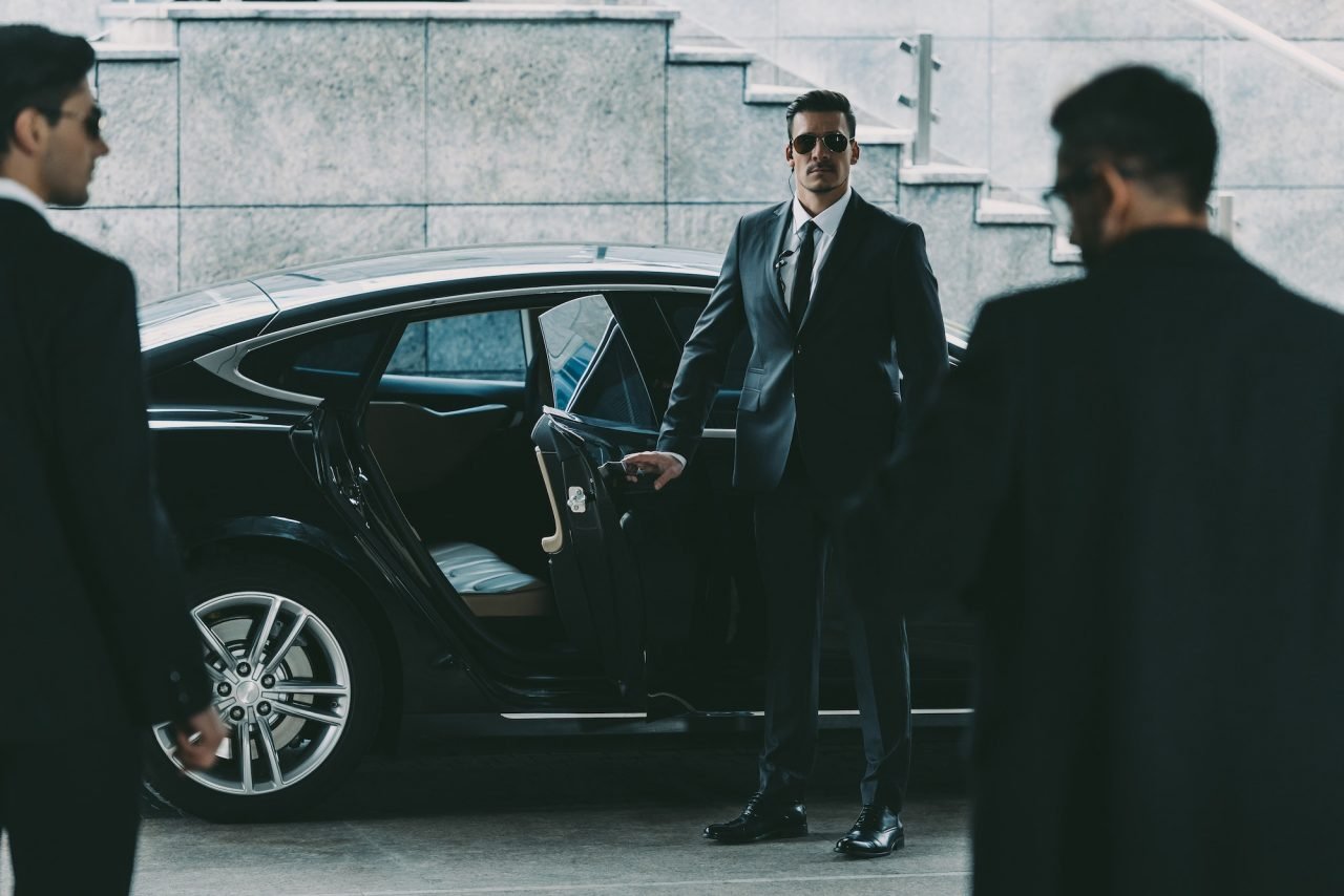 Bodyguard in sunglasses opening a car door for a business client