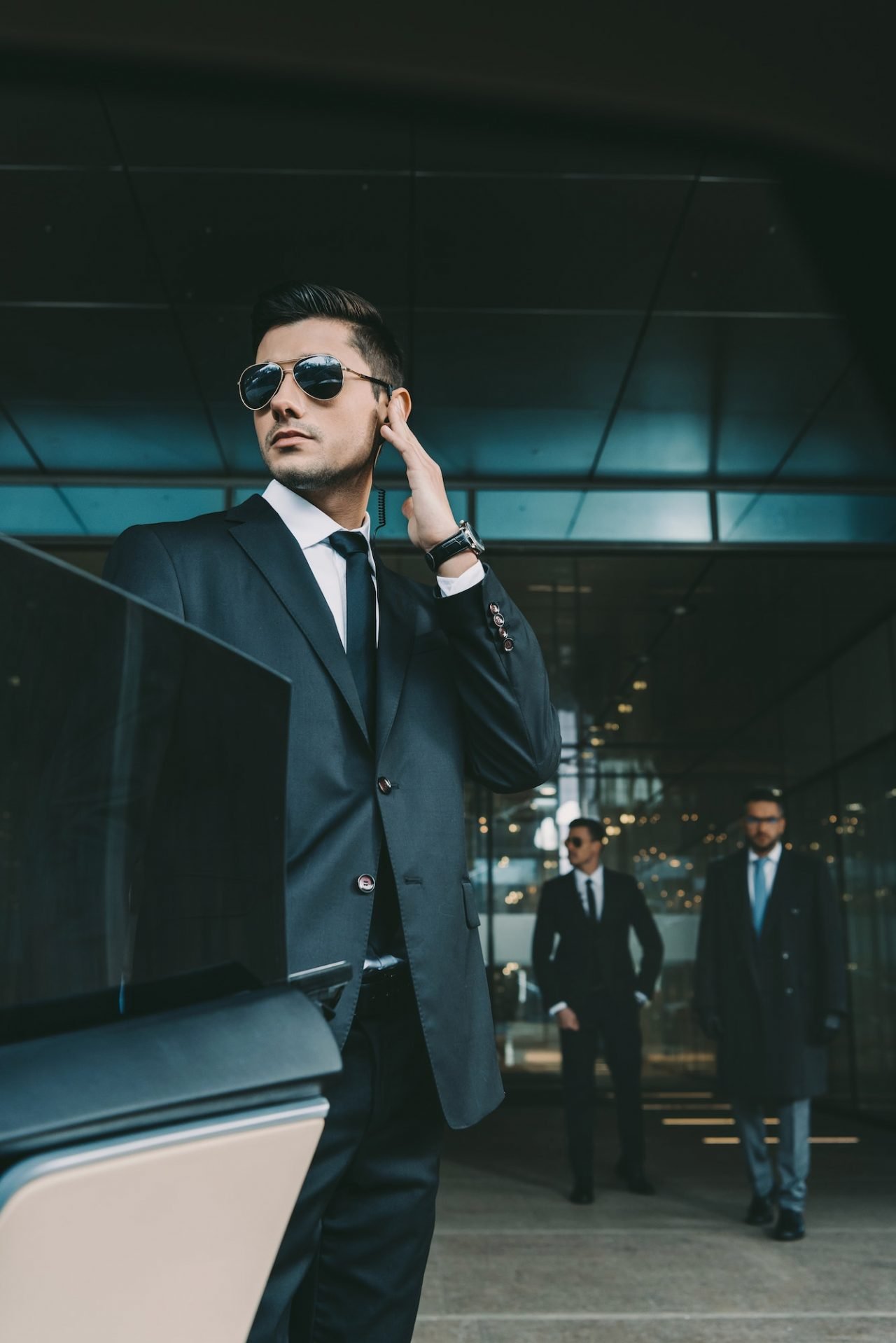 Bodyguard with a security earpiece opening a car door for a client